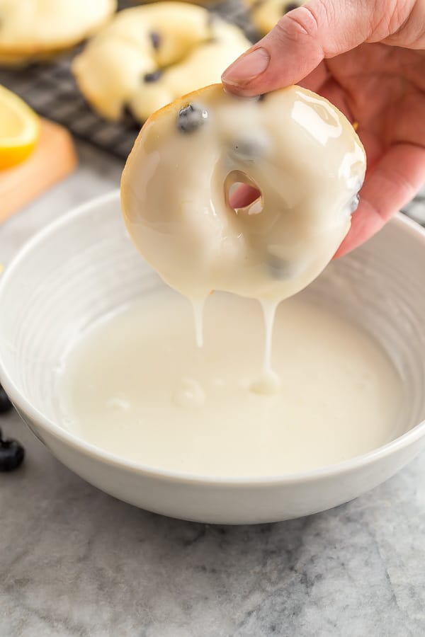 lemon baked donut being dunked in lemon glaze
