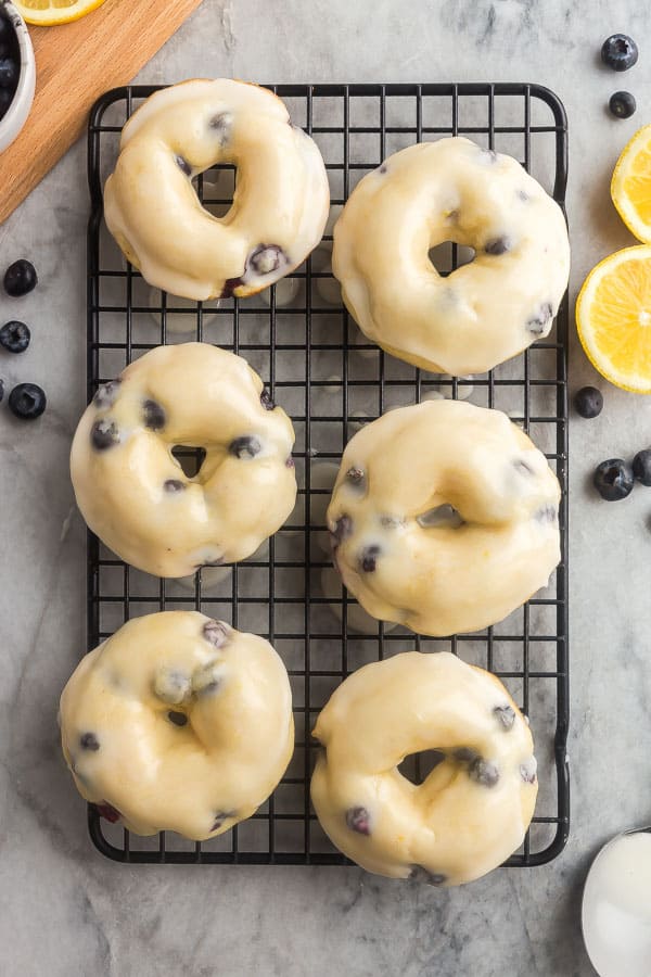 These Baked Lemon Blueberry Donuts are fluffy, packed with citrus flavor and bursting with blueberries and covered in a tangy glaze! Baked donuts are the perfect healthy breakfast or snack. Includes step by step recipe video. #donuts #baking #dessert #lemon overhead image of 6 baked donuts with glaze