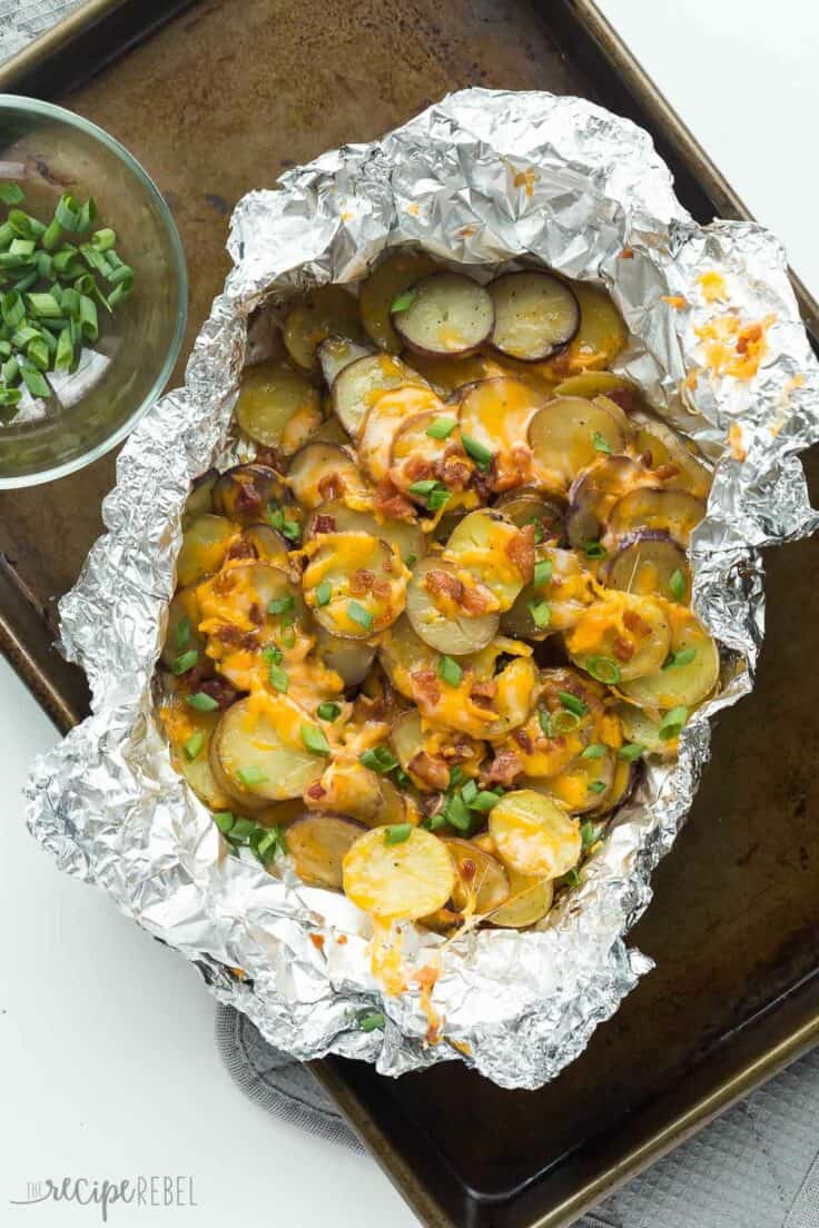 cheesy grilled potatoes with bacon in foil pack topped with green onions on sheet pan