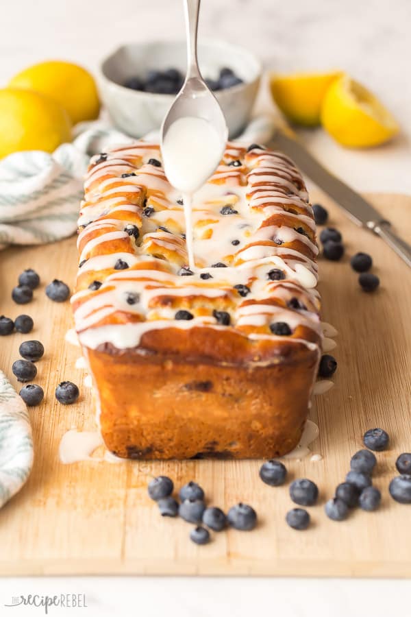 This Blueberry Lemon Bread is sweet, tangy, loaded with juicy blueberries and a decadent cream cheese swirl! It's the perfect quick bread recipe for Spring! #lemon #blueberries #bread #baking #recipe blueberry lemon bread drizzled with glaze on wood cutting board