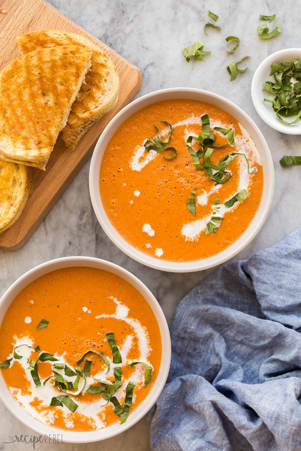 overhead image of two bowls of roasted tomato soup with grilled cheese on the side