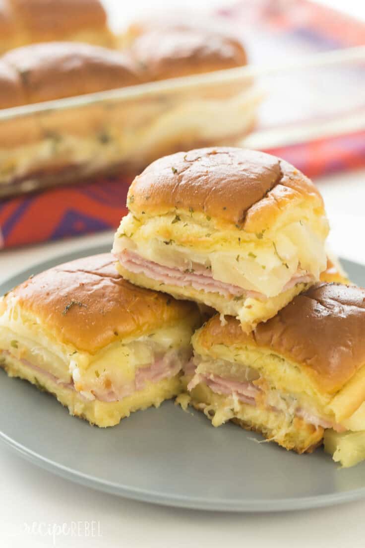 hawaiian ham and pineapple sliders stacked on grey plate in front of baking dish