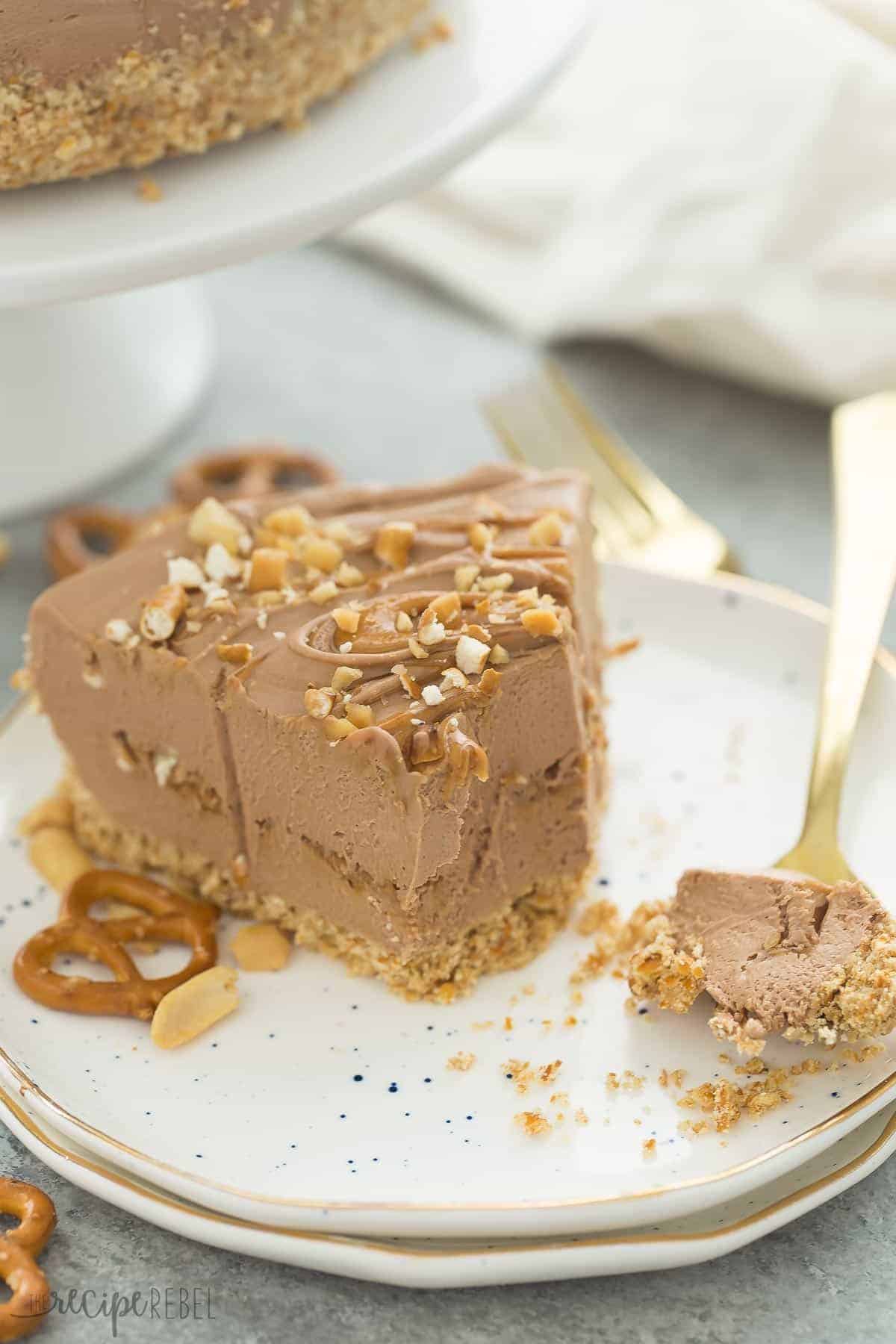 slice of peanut butter pretzel cheesecake on white speckled plate with bite on fork