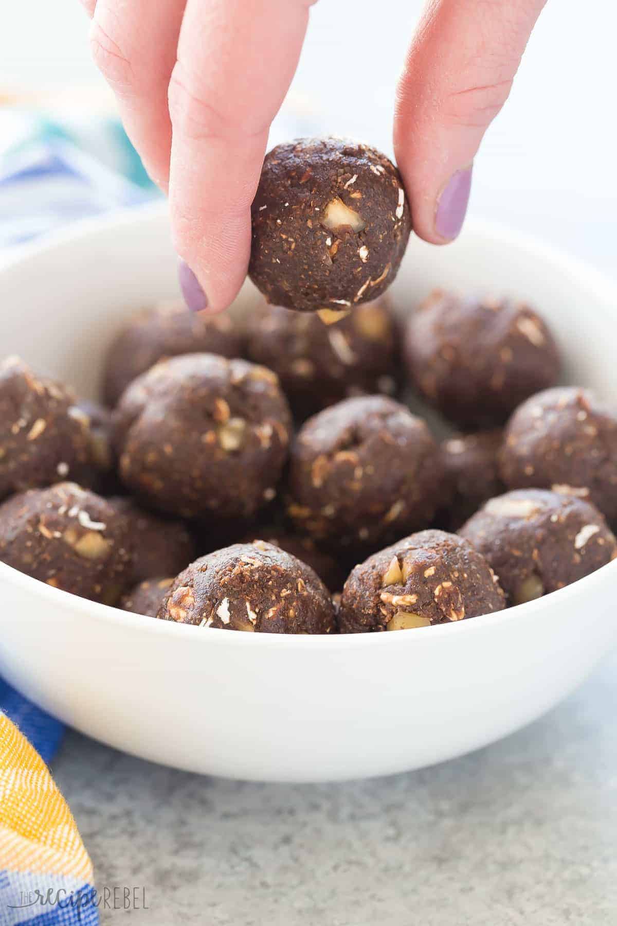 chocolate hazelnut energy bites in bowl with hand picking up one energy bite