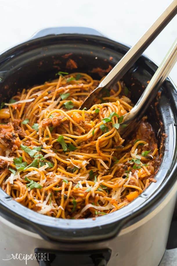 healthier ground beef crock pot spaghetti in black slow cooker with meal tongs pulling some out