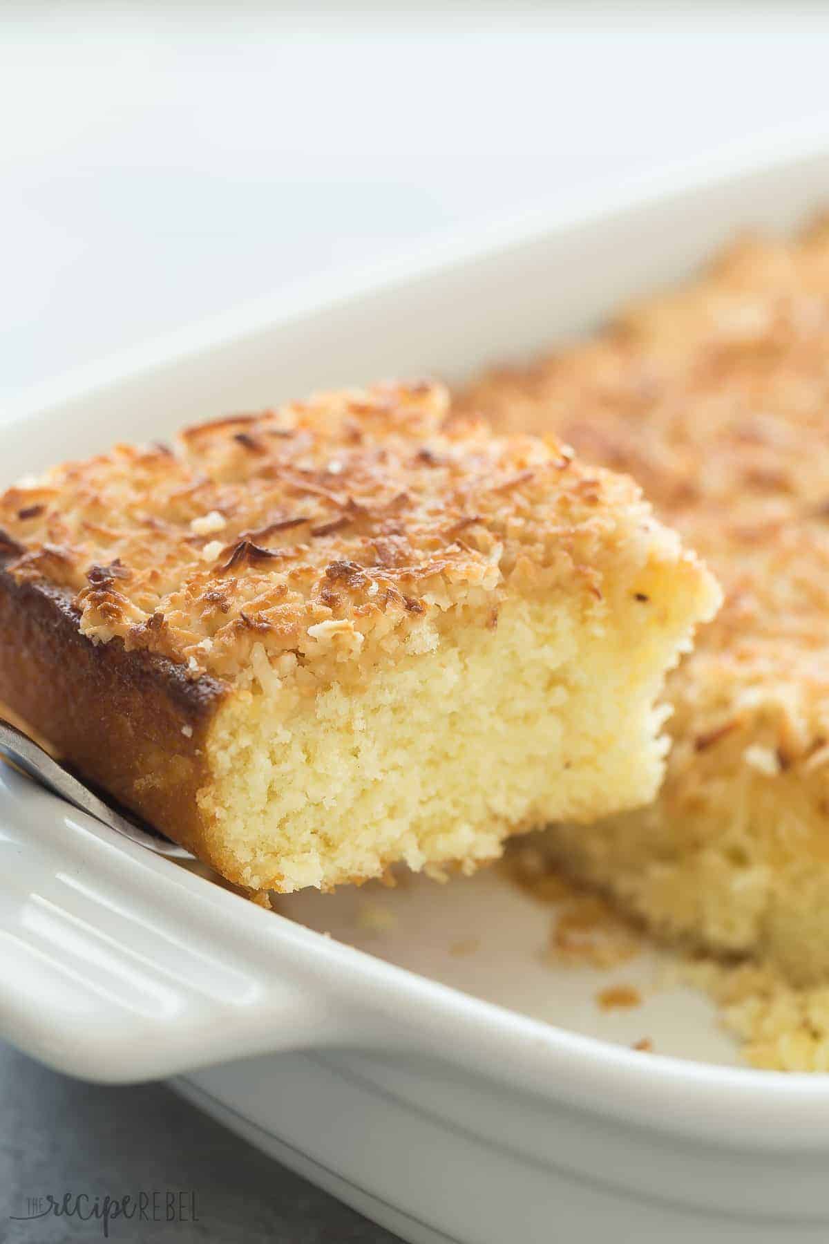 piece of hot milk cake being removed from white baking dish with spatula