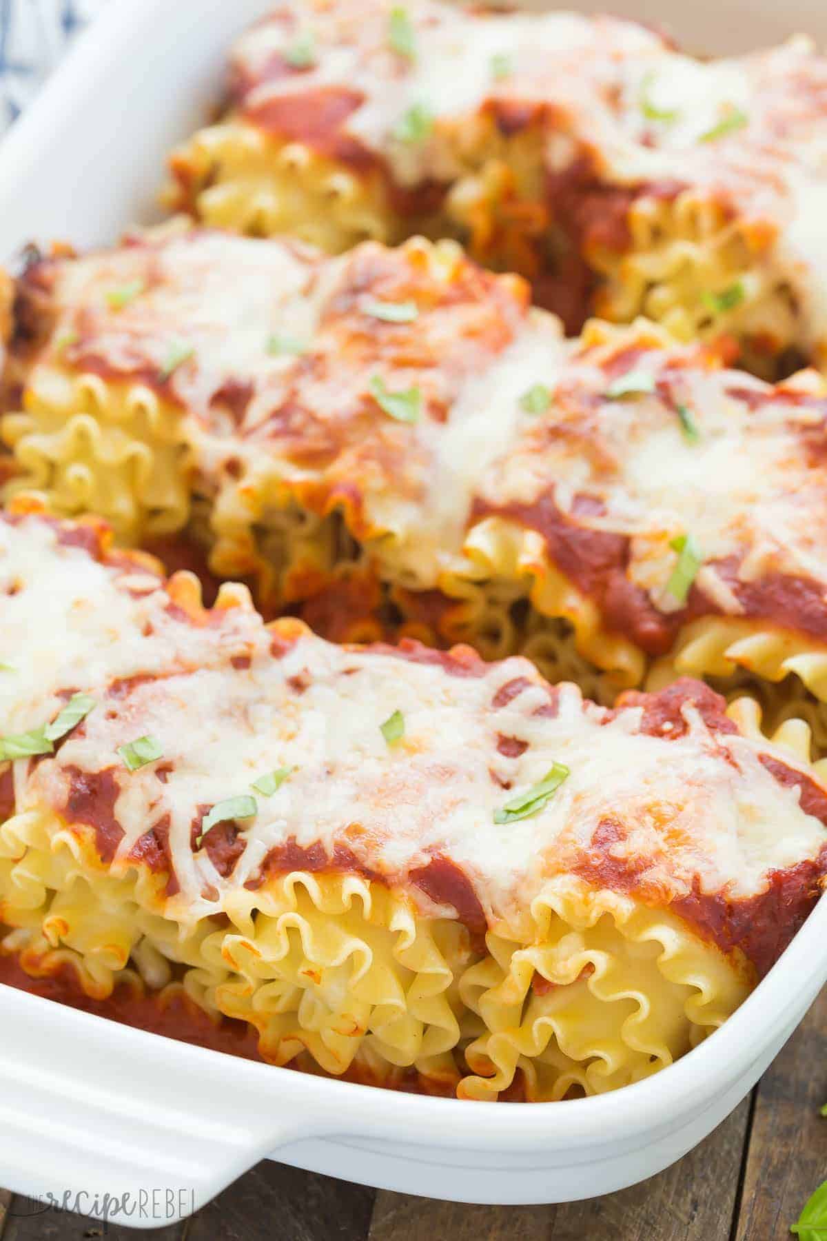 pepperoni pizza roll ups in white baking dish topped with tomato sauce and cheese