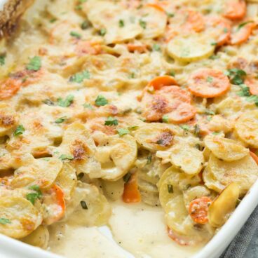 scalloped potatoes and carrots in white baking dish with scoop missing from corner