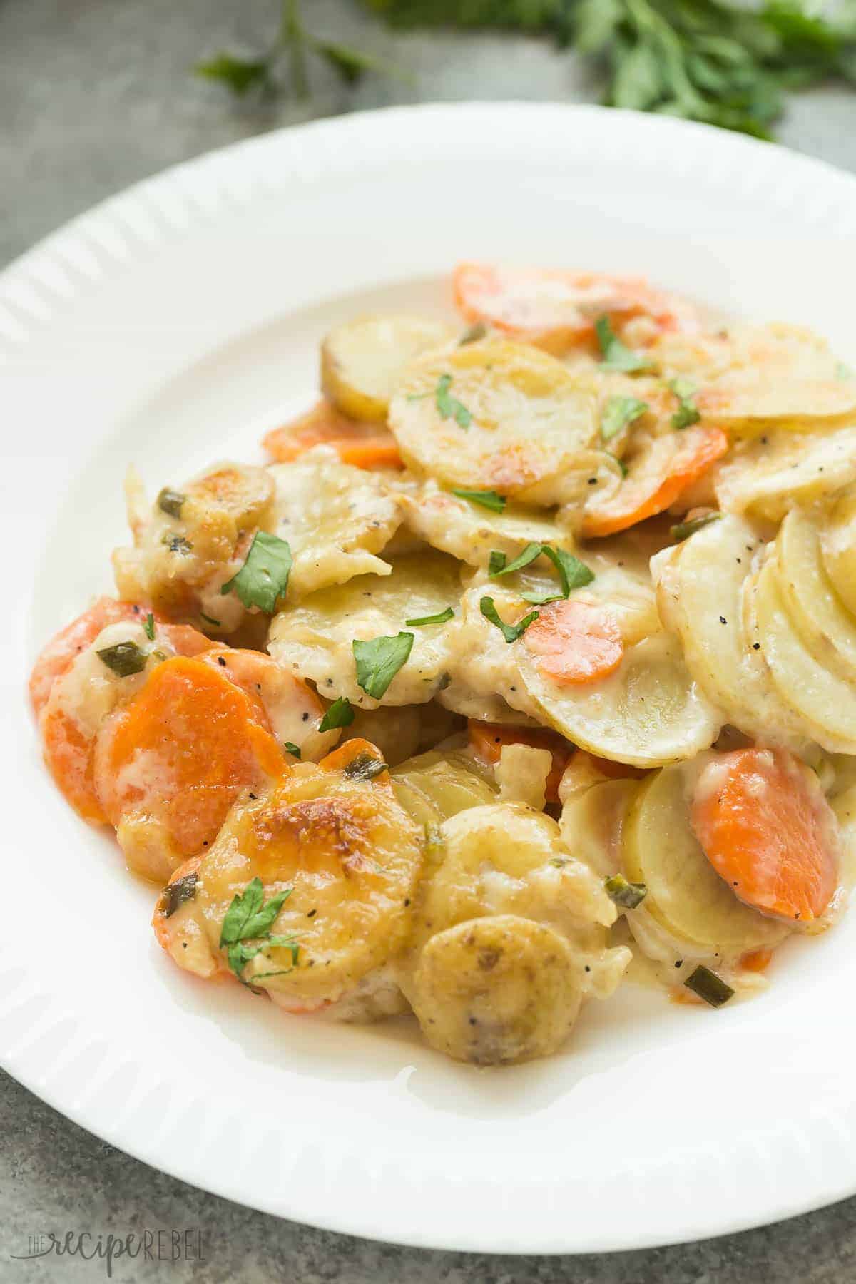 white plate with scalloped potatoes and carrots and sprinkled with fresh parsley