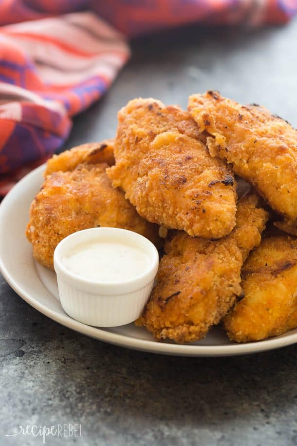 crispy sriracha oven fried chicken stacked on a white plate with a small bowl of ranch on the side