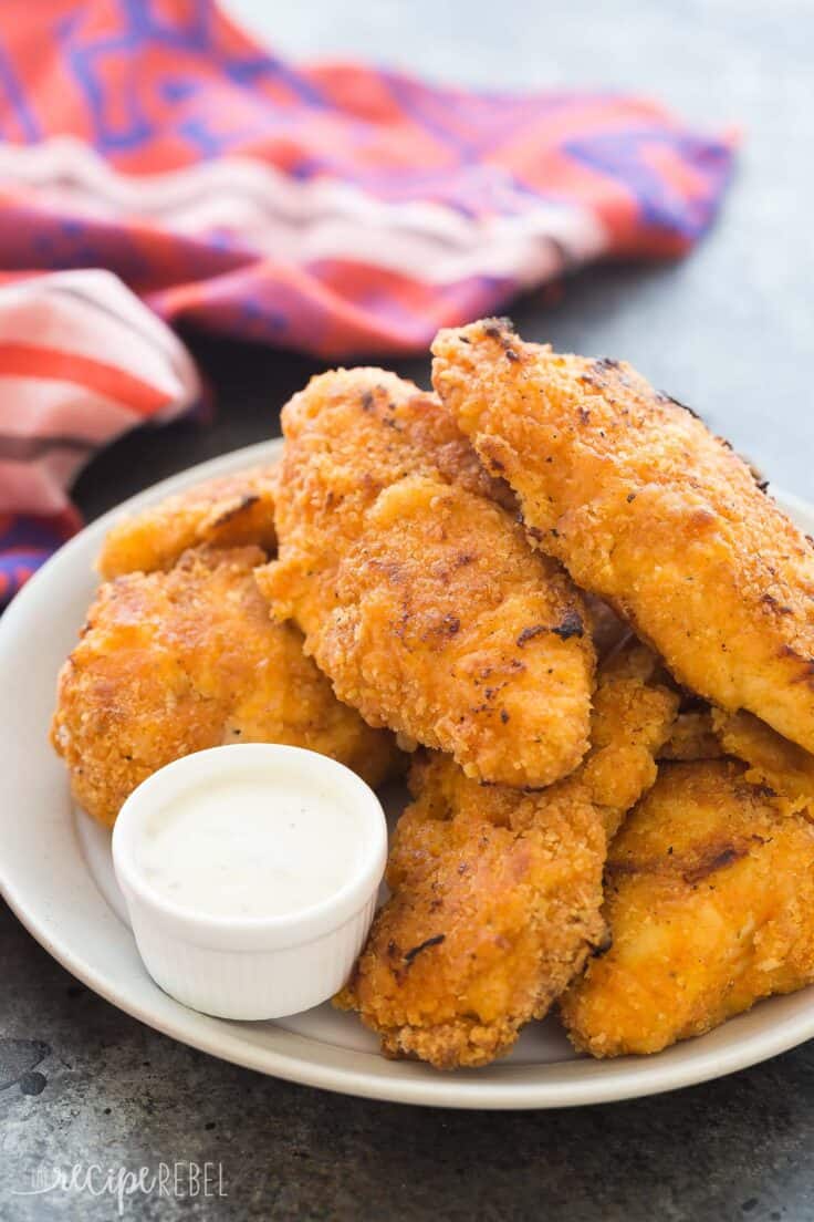 This Crispy Sriracha Buttermilk Oven Fried Chicken is so moist and juicy with just the right amount of spice! It's baked and not fried so it's healthier, but you still get that great crunchy coating. Includes a step by step recipe video. sriracha buttermilk oven fried chicken piled on plate with small bowl of ranch dip