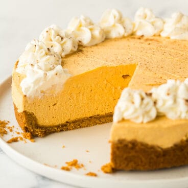 whole no bake pumpkin cheesecake on white plate with one piece cut out