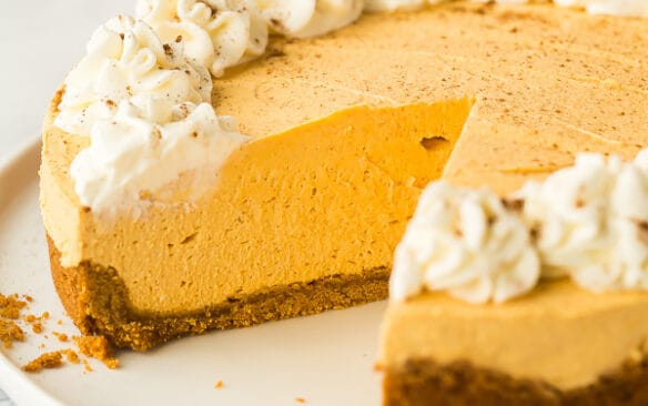 whole no bake pumpkin cheesecake on white plate with one piece cut out