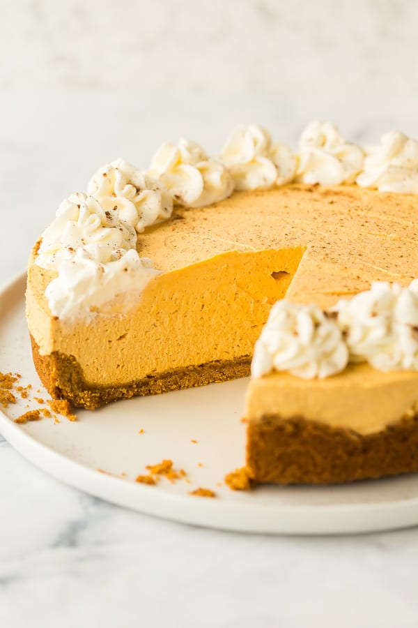 whole no bake pumpkin cheesecake on white plate with one piece cut out