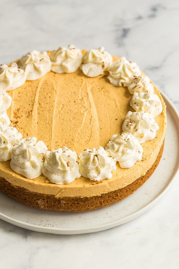 This No Bake Pumpkin Cheesecake is light, airy and so easy to make -- the perfect pumpkin dessert for a fall supper or Thanksgiving #pumpkin #cheesecake #dessert #recipe no bake pumpkin cheesecake whole on white plate with whipped cream