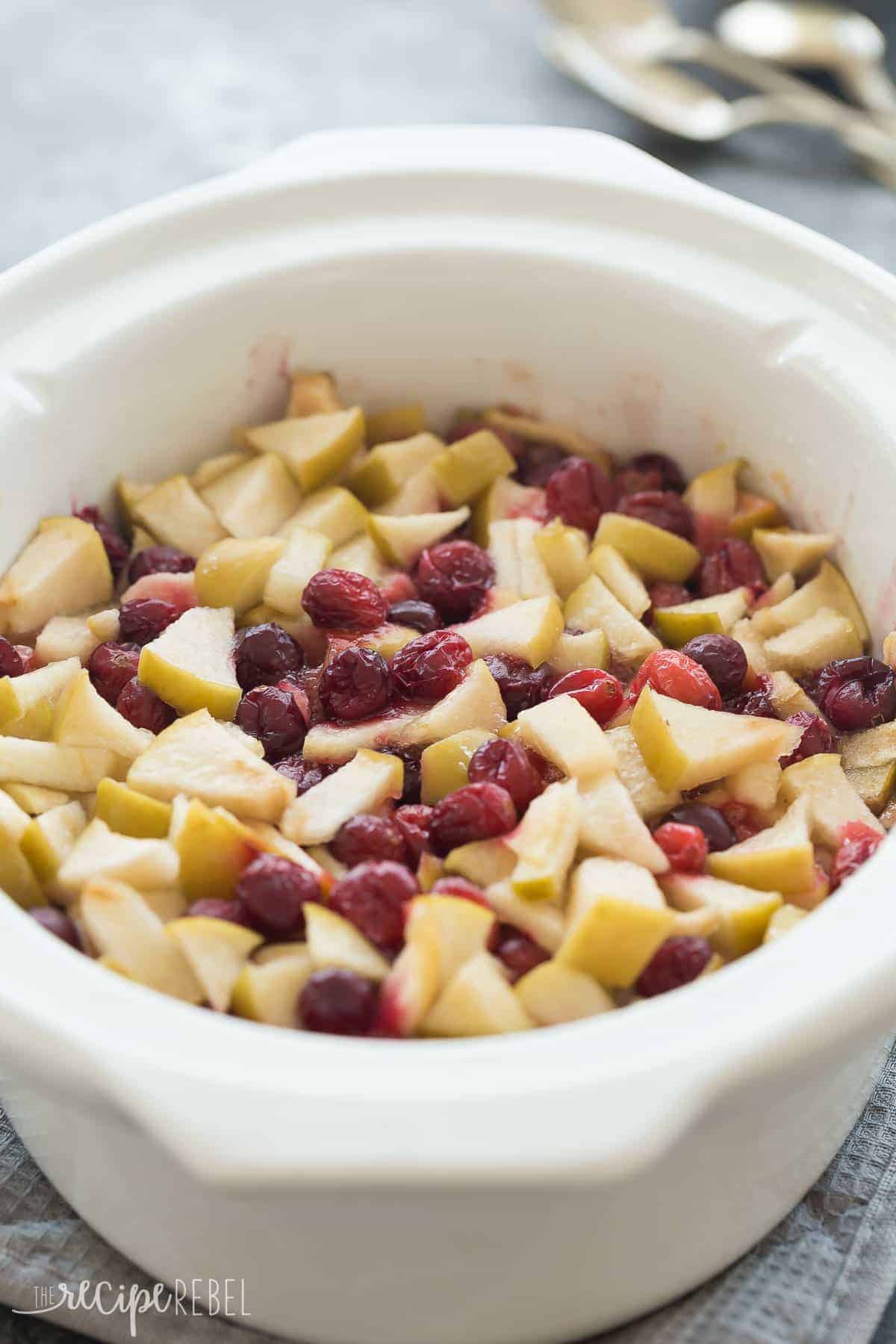 white slow cooker with cobbler and apples and cranberries on top