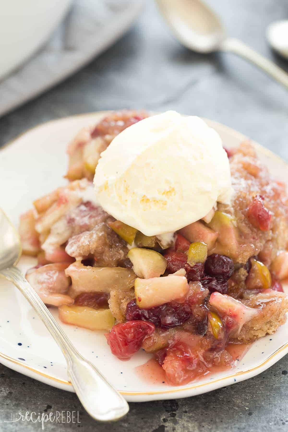 cranberry apple cobbler on white speckled plate with vanilla ice cream