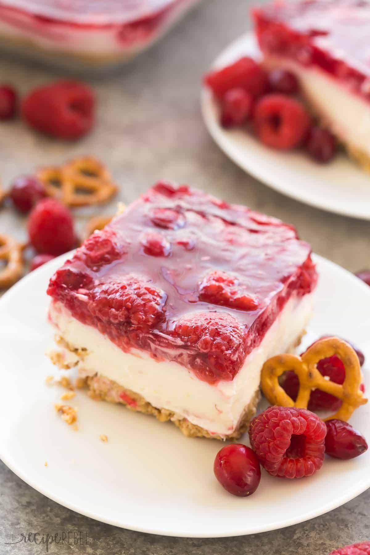 piece of cranberry raspberry pretzel salad on white plate with raspberries and pretzels in the background