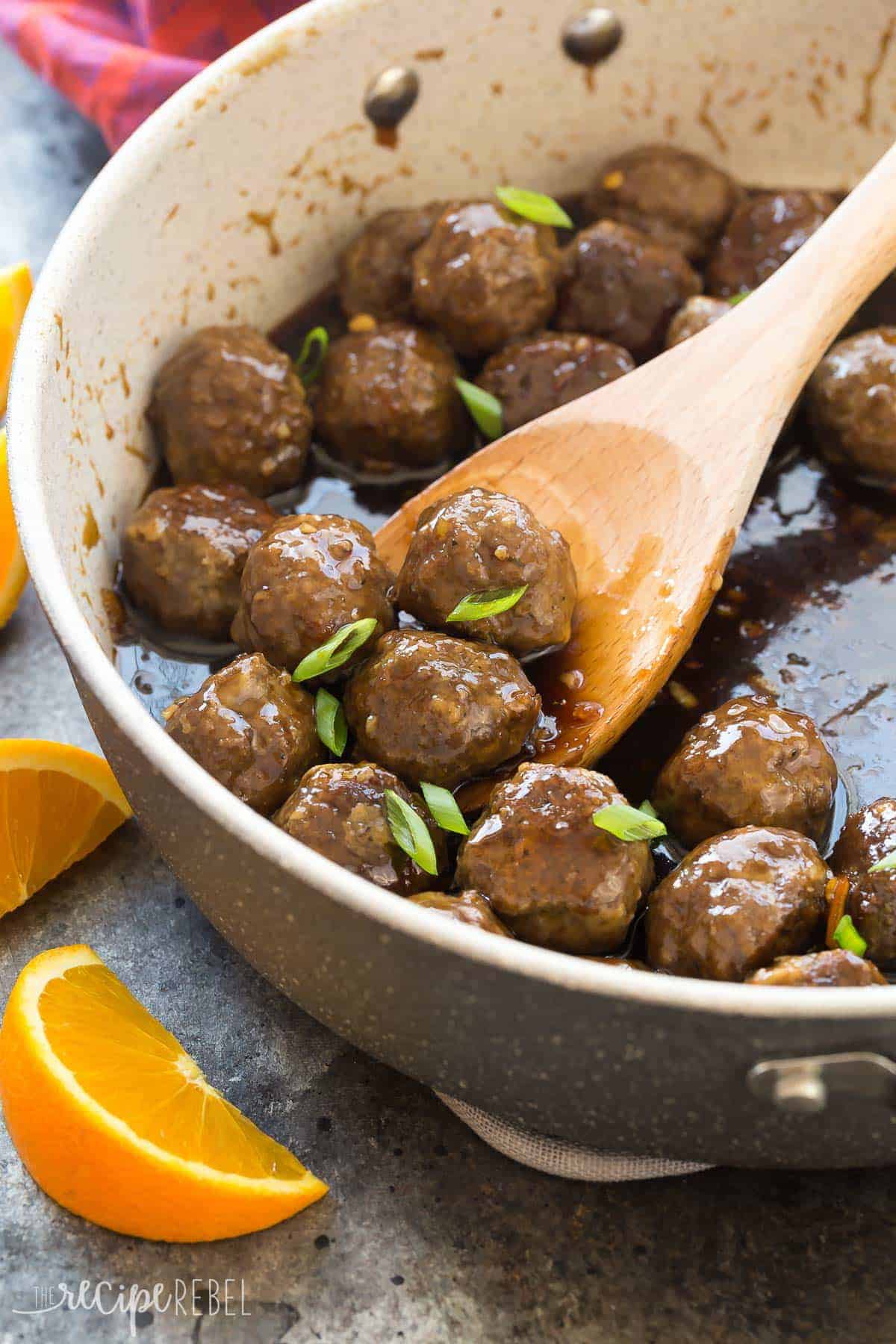 meatballs in large grey skillet with orange sauce and wooden spoon scooping meatballs