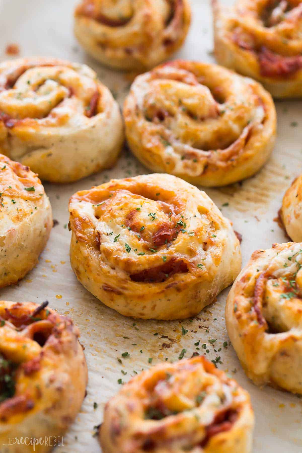 pizza pinwheels on parchment lined baking sheet sprinkled with dried parsley