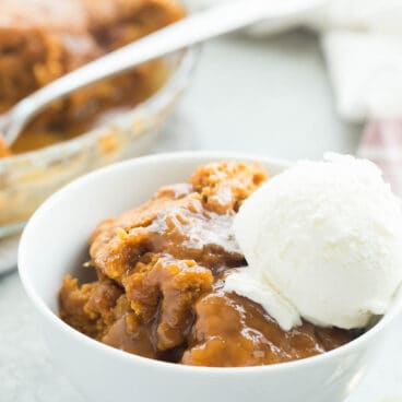 pumpkin pudding cake in small white bowl with scoop of vanilla ice cream and spoons on the side