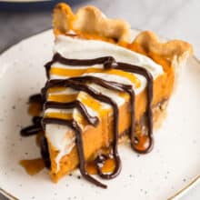 slice of pumpkin pie on white plate with chocolate and caramel drizzle