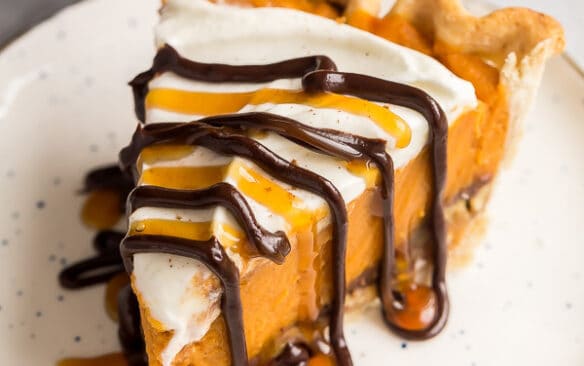 slice of pumpkin pie on white plate with chocolate and caramel drizzle