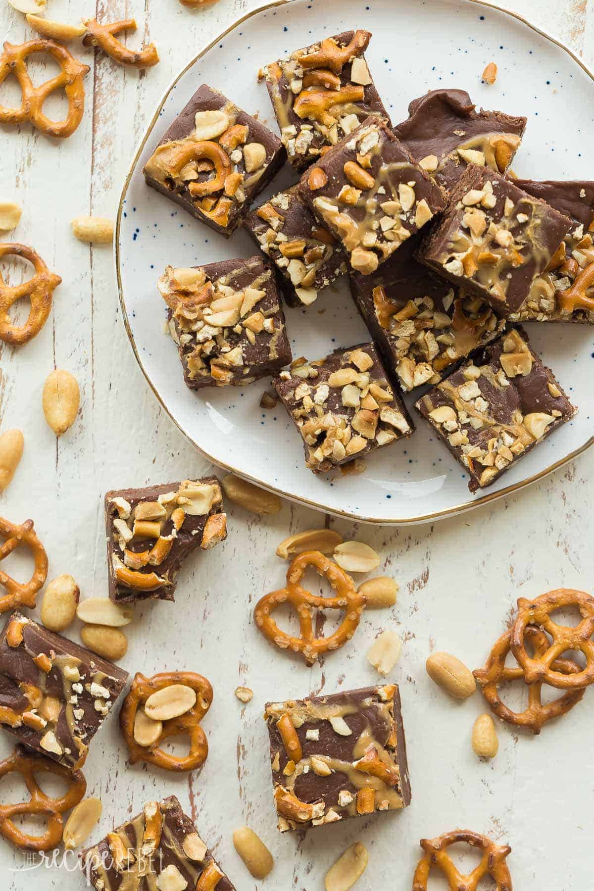 overhead image of pieces of peanut butter pretzel fudge on white plate with pretzels and peanuts all around