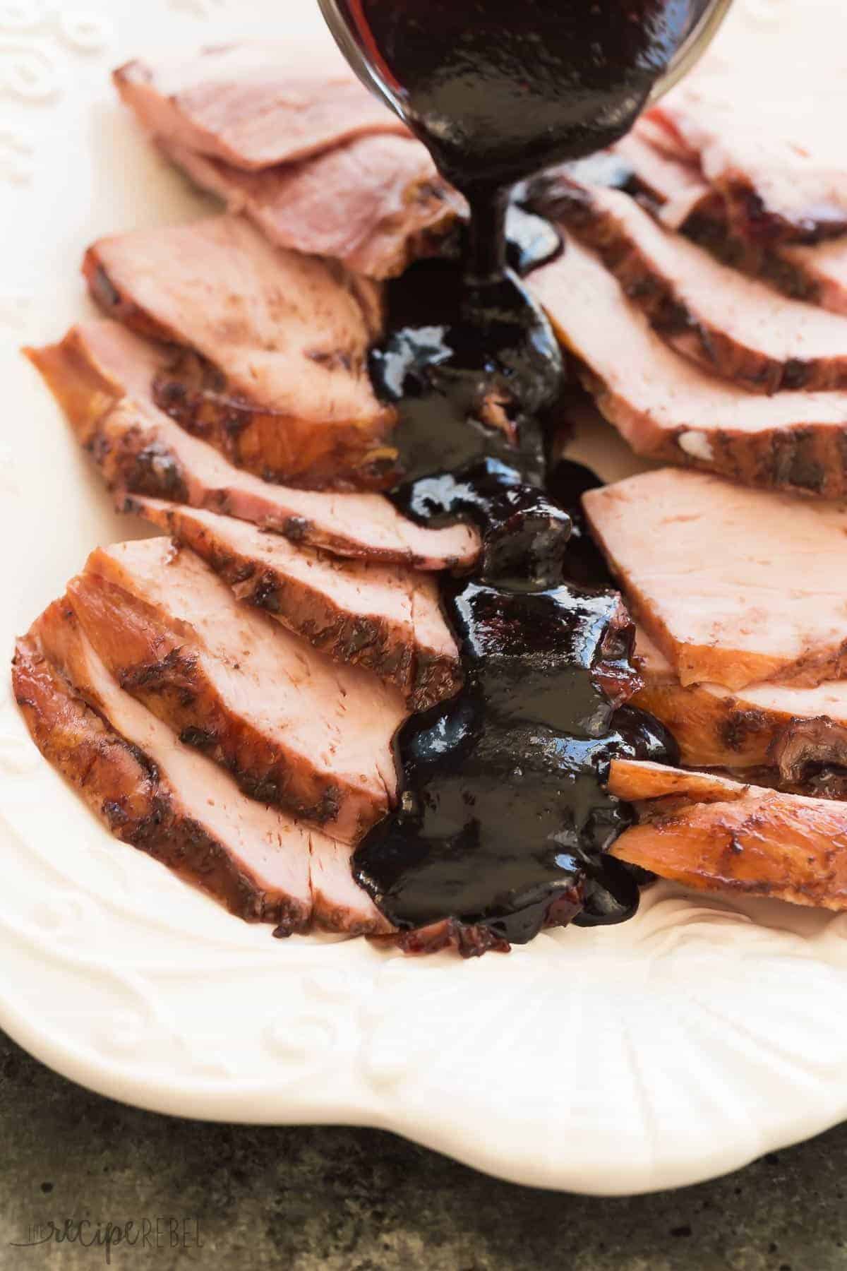 slices of ham on white platter with thick drizzle of cherry glaze down the middle