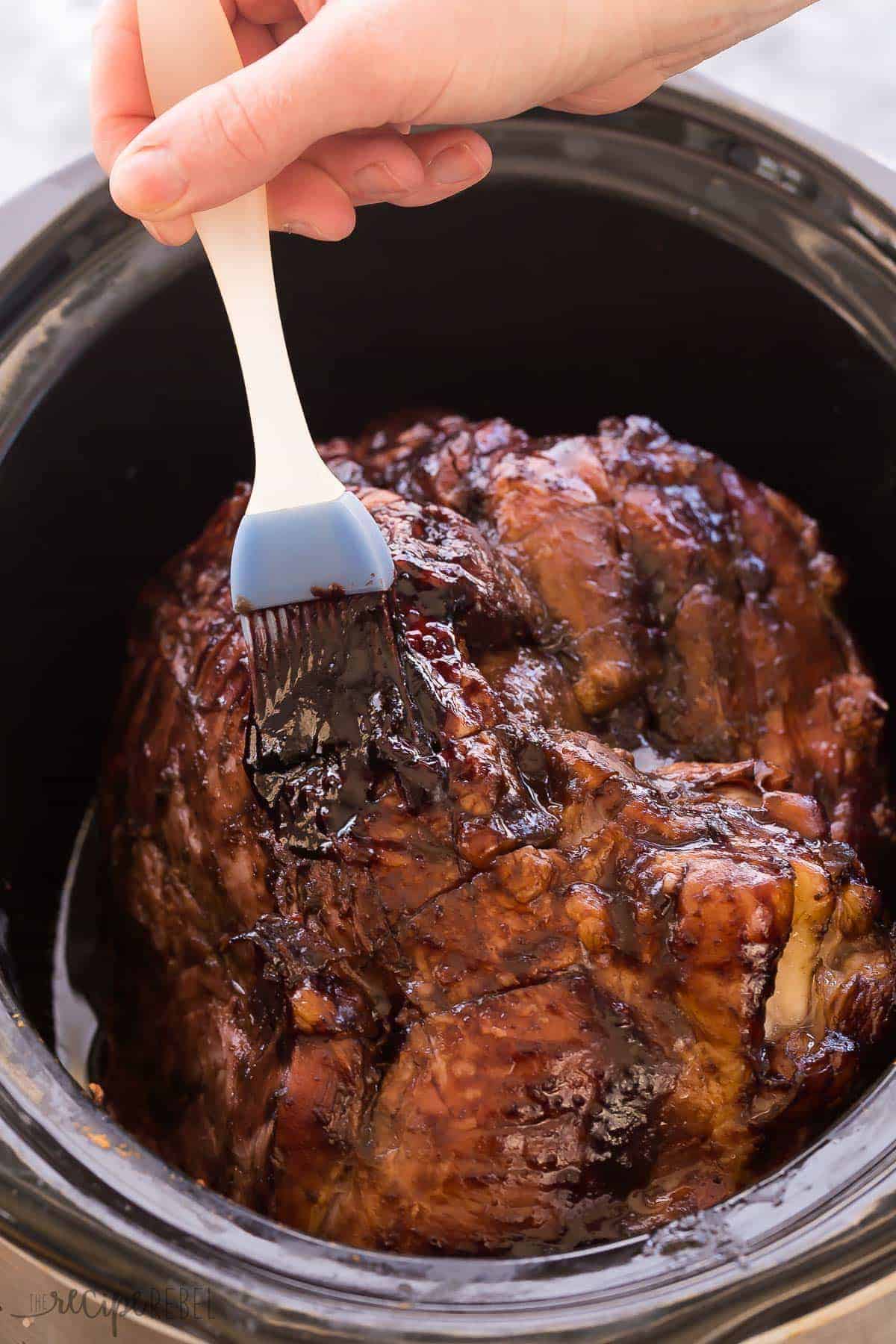 whole ham in black slow cooker being brushed with cherry glaze