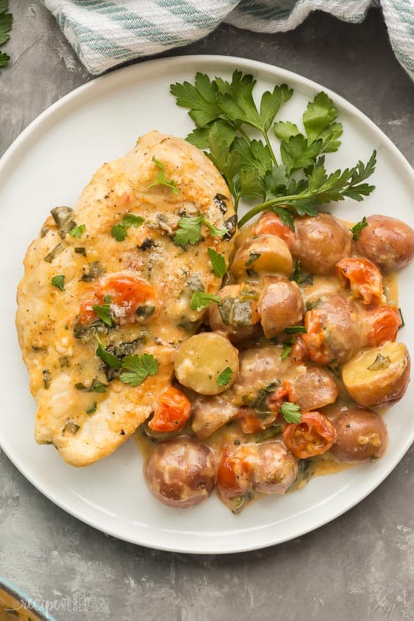 tuscan chicken and potato skillet on white plate with fresh parsley on grey background