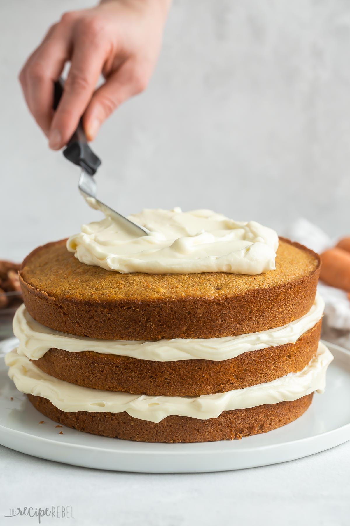 cream cheese frosting being spread on top layer of carrot cake