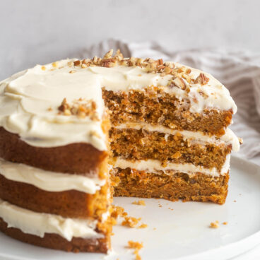 three layer carrot cake with cream cheese frosting in between layers and slices cut out