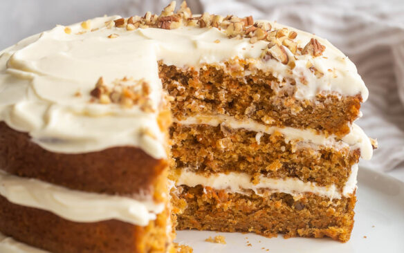 three layer carrot cake with cream cheese frosting in between layers and slices cut out
