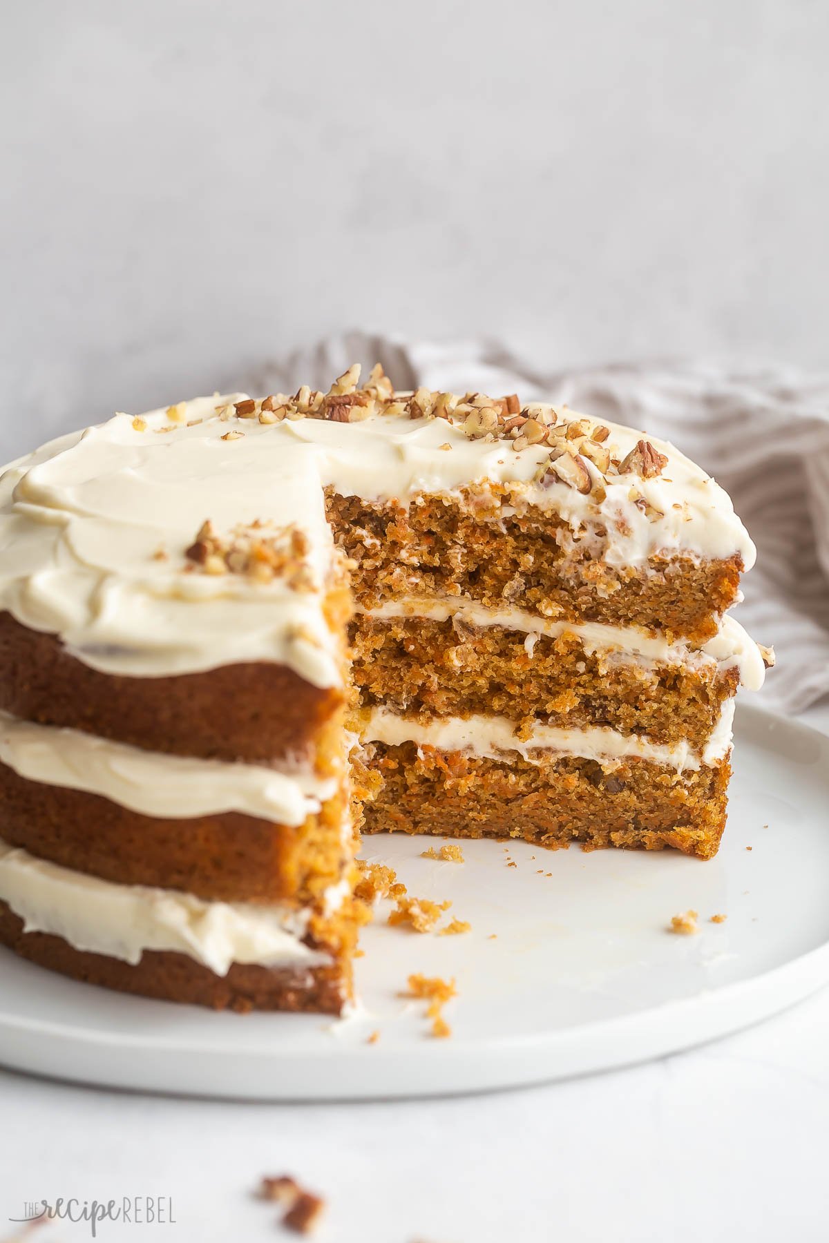 three layer carrot cake with cream cheese frosting in between layers and slices cut out