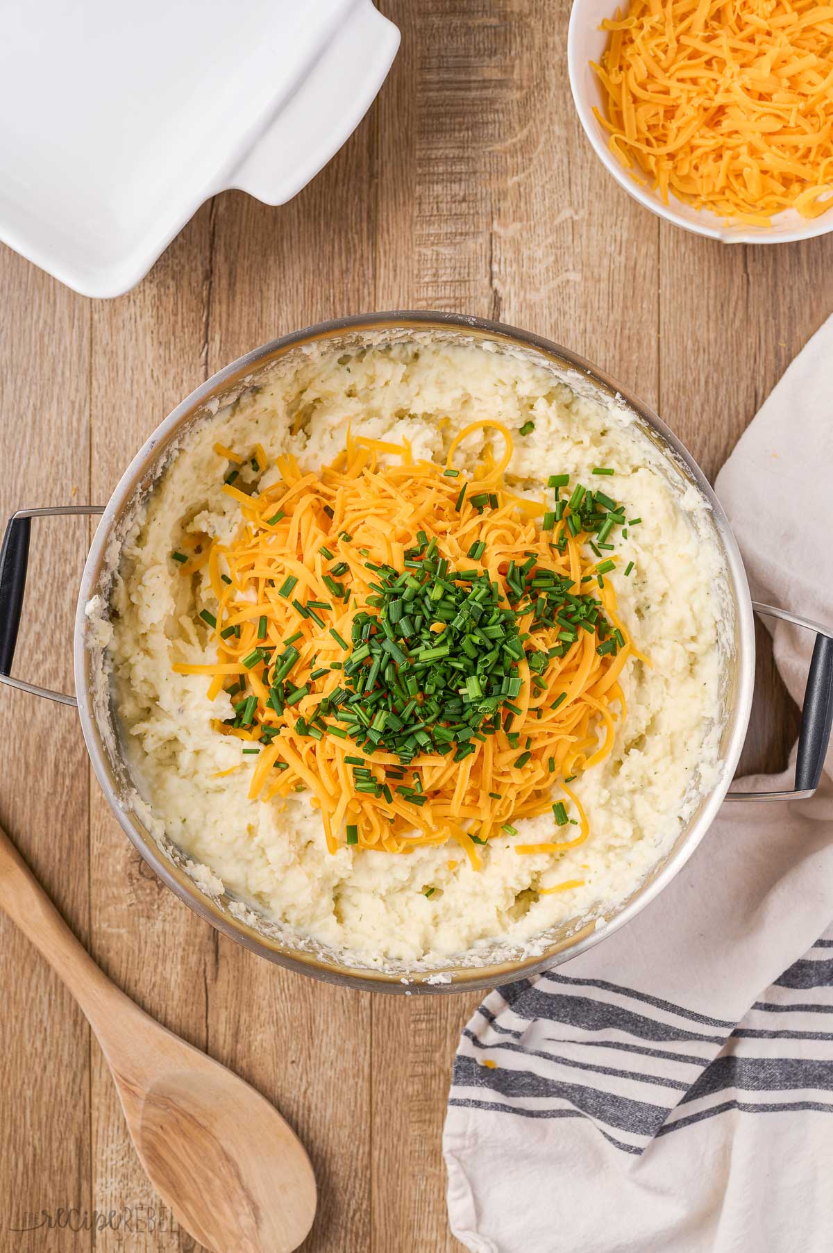 adding shredded cheese and chives to mashed potatoes