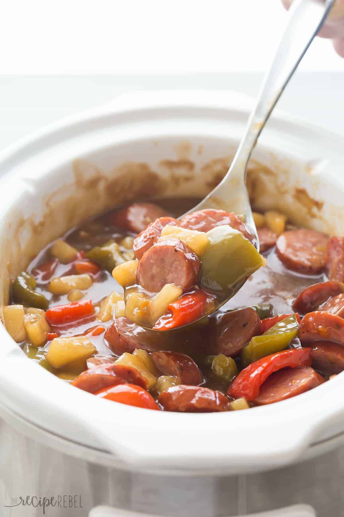 sweet and sour smokies in white crockpot with metal spoon scooping some