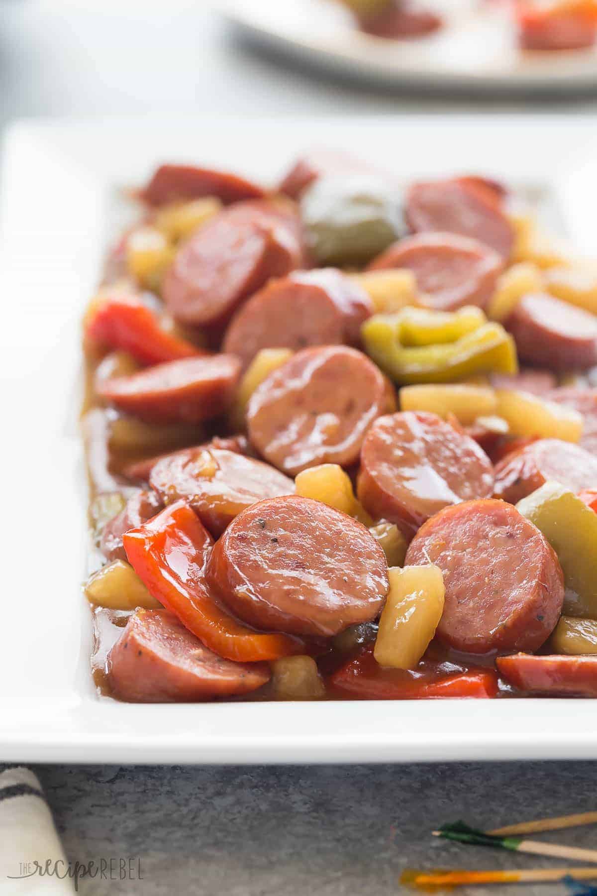 a long white plate with sliced smokies in sweet and sour sauce with pineapple and peppers