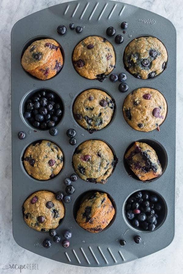 blueberry oatmeal muffins in muffin pan overhead on marble background with fresh blueberries