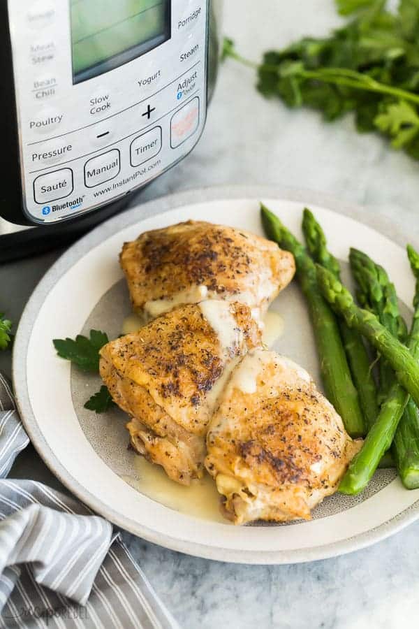 pressure cooker chicken thighs on grey and white plate with asparagus and instant pot in the background