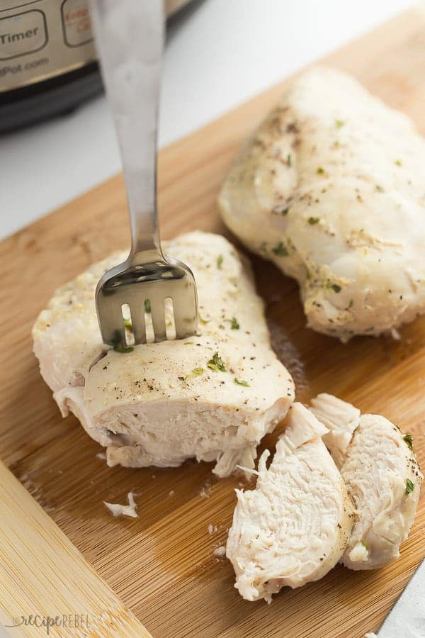 chicken breasts on cutting board being sliced in front of the instant pot