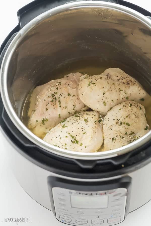 cooked chicken breasts in instant pot with seasonings and fresh herbs on top