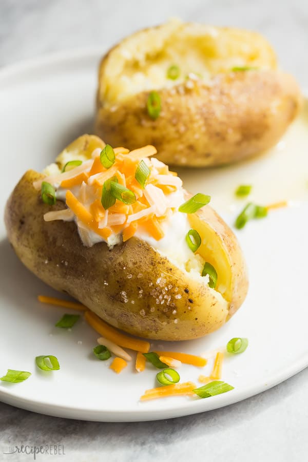 instant pot baked potatoes on white plate close up with sour cream shredded cheese and green onions