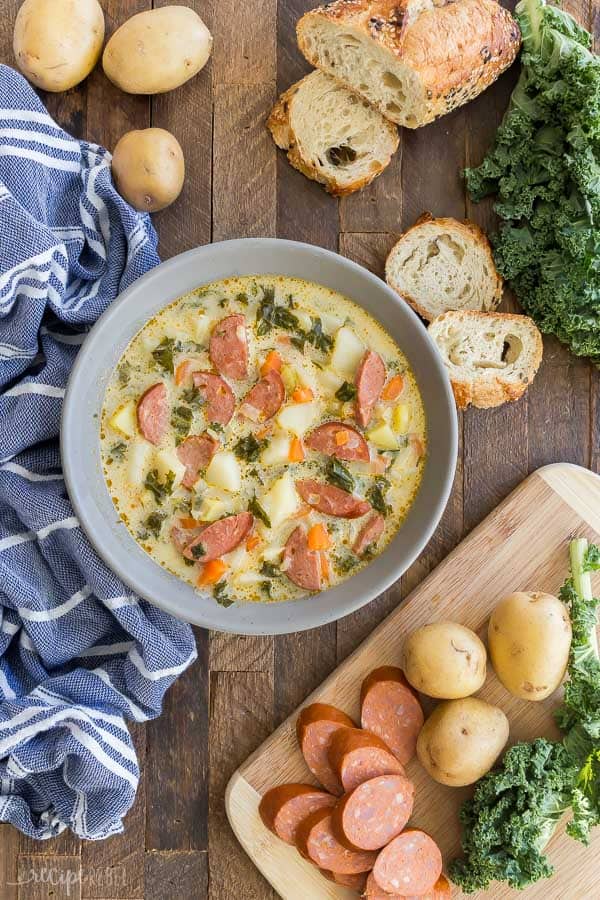 sausage potato kale soup overhead in grey bowl with crusty bread on the side