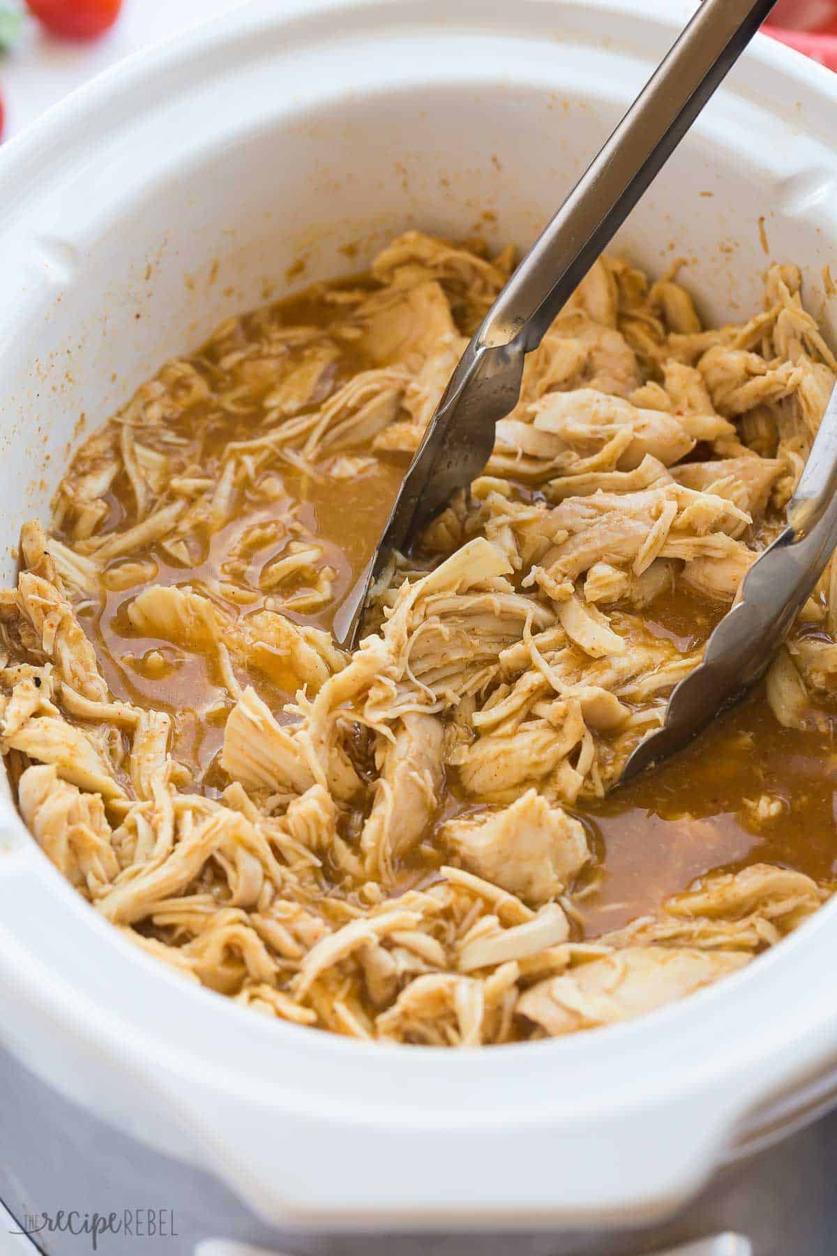 sweet and spicy chicken taco meat shredded in crockpot with metal tongs