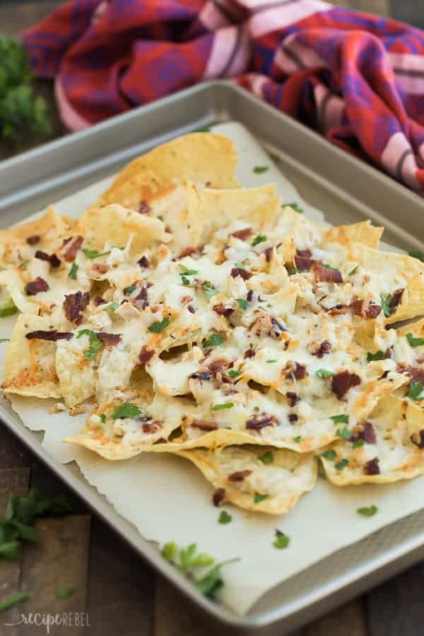 close up image of chicken alfredo nachos on sheet pan on wood background