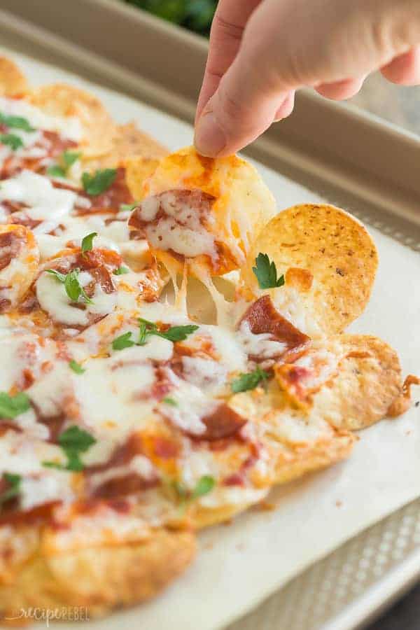 close up image of a hand pulling out a pepperoni pizza nacho from sheet pan