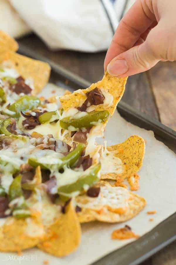 close up image of hand pulling up philly cheesesteak nacho from baking sheet