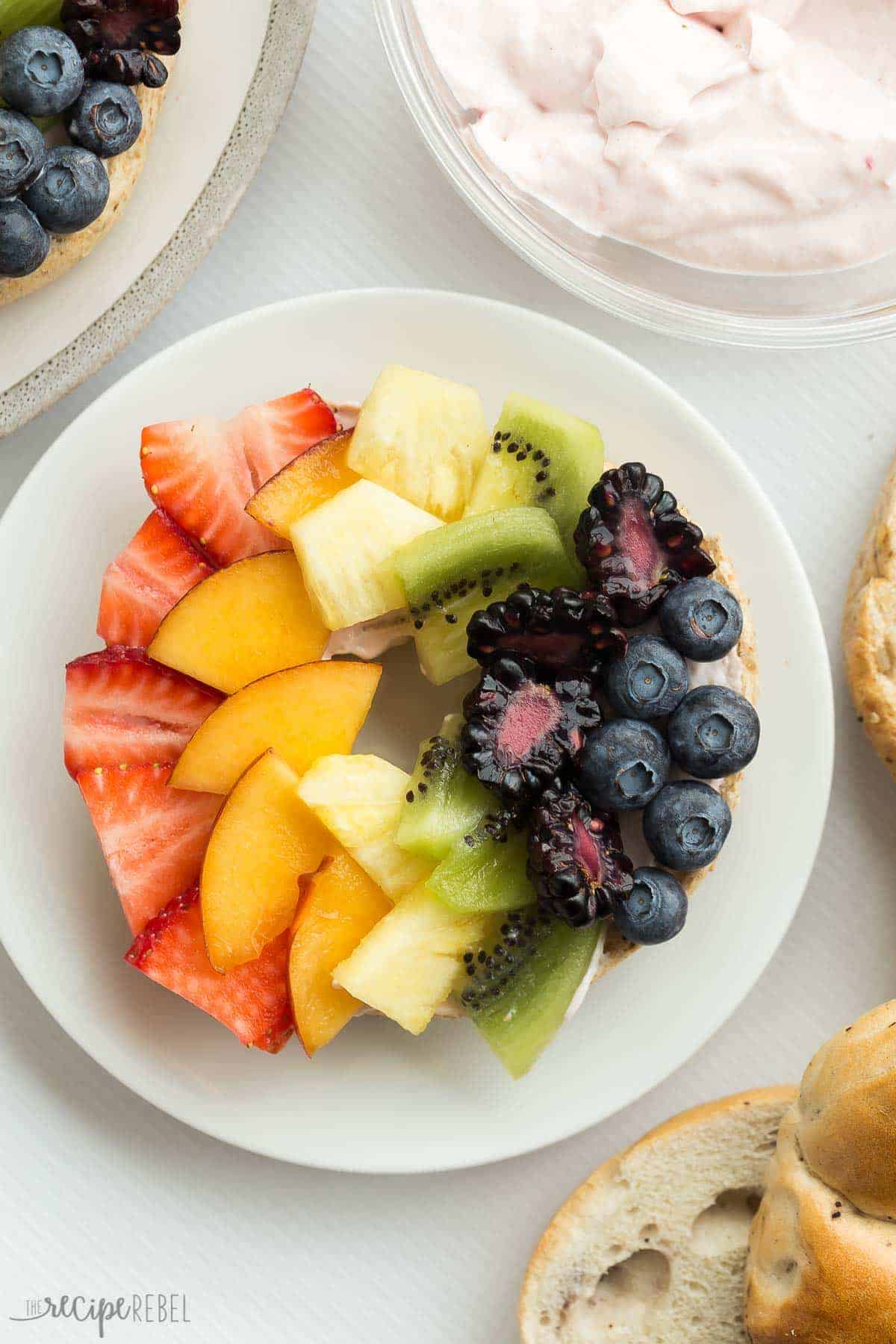 These Rainbow Bagel Fruit Pizzas with Strawberry Cream Cheese Spread are a fun breakfast or snack! Topped with a homemade, naturally sweetened strawberry cream cheese spread and fresh fruit that the kids (and the rest of the family!) will love! A fun treat for Easter, St. Patrick's Day or any day! Includes step by step recipe video. #rainbowfood rainbow food #fruit #breakfast #brunch #creamcheese 