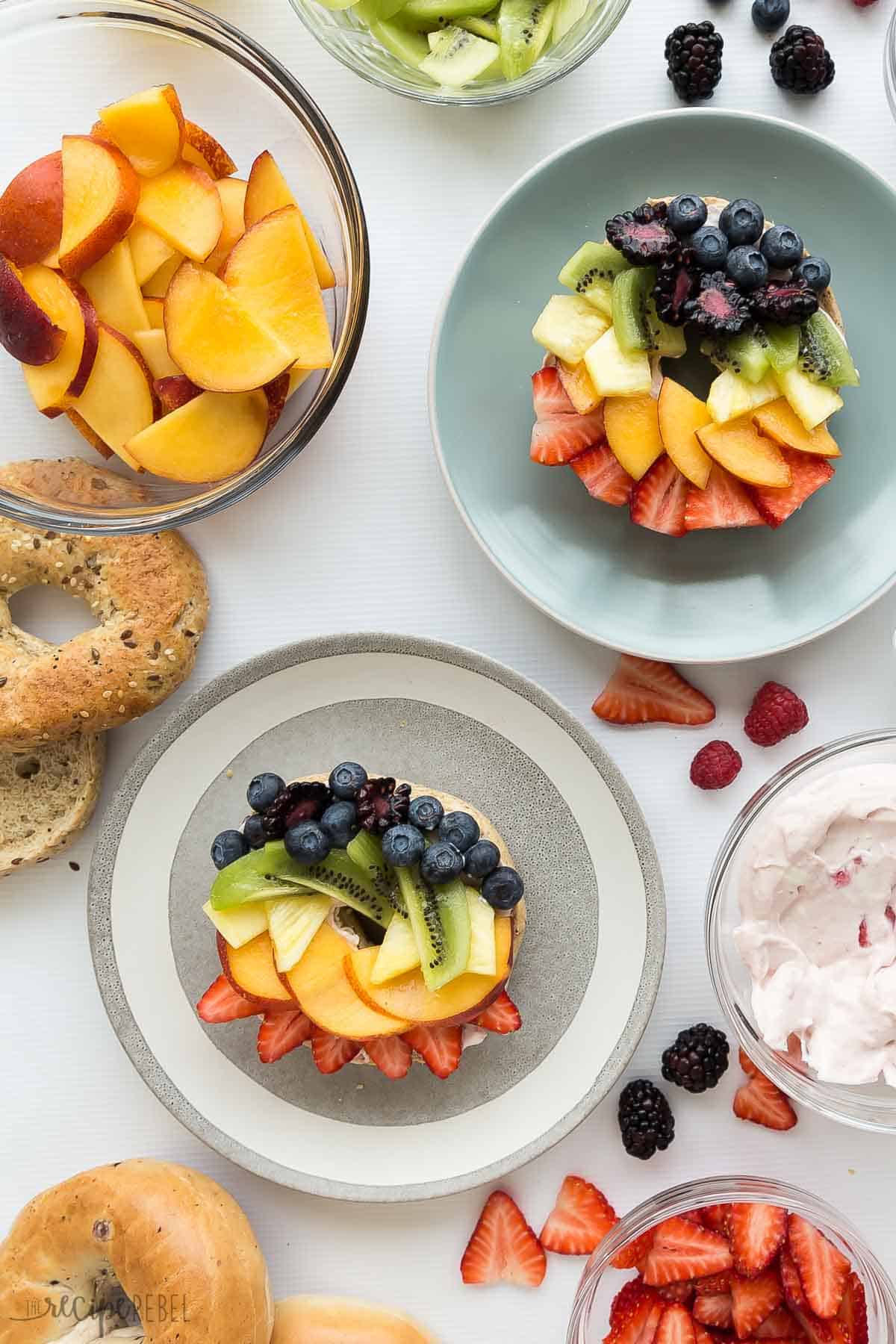 overhead image of two rainbow fruit pizza bagels with extra bagels peaches and strawberries on the side